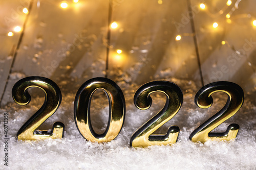 Gold numbers 2022 on wood background with snow and luminous garland. New year backdrop with 2022 year photo