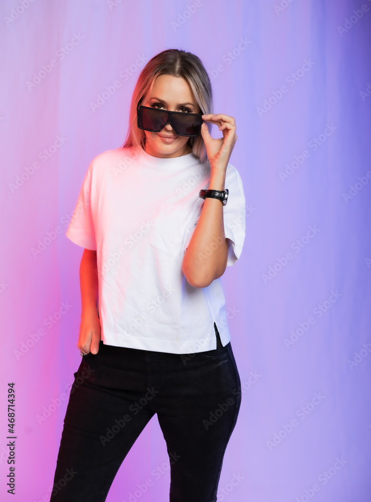 Woman in white t-shirt, black jeans and sunglasses on colorful background Woman in white t-shirt, black jeans and sunglasses on colorful background