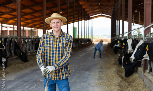 Portrait of confident man cow breeder standing in outdoor cowshed on sunny summer day