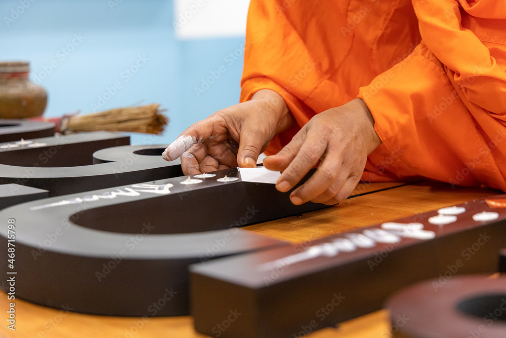 Thai monk to bless by making marks on the sign with golden leaf for lucky in rite of Thai traditional ceremony. Monk anoints holy powder on a text sign. Thai monk to bless by making marks on the sign with golden leaf for lucky in rite of Thai traditional ceremony. Monk anoints holy powder on a text sign.