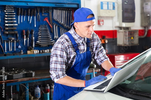 Mechanic man manager using a laptop computer checking car in workshop at auto car repair service center