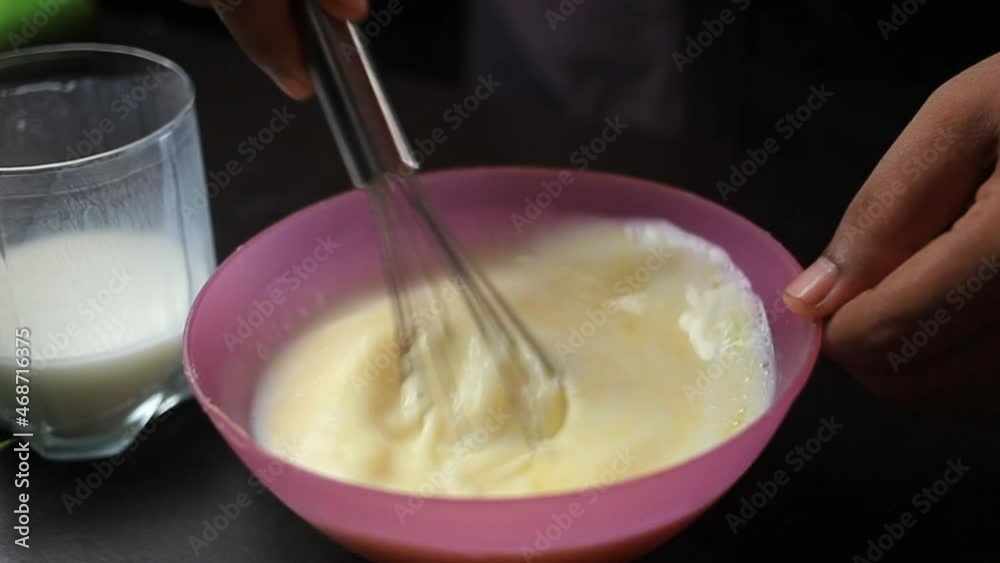 Stirring egg and buttermilk in a purple coloured mixing bowl with whisk by hand