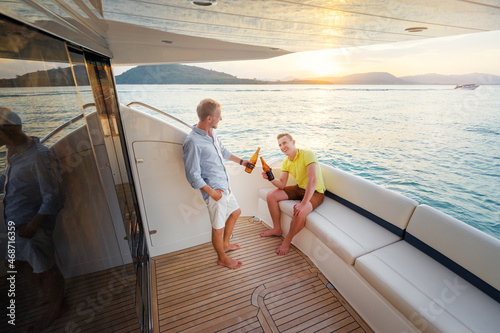 Friendship and vacation. Two young handsome men talking and drinking beer on the yacht sailing the sea. © luengo_ua