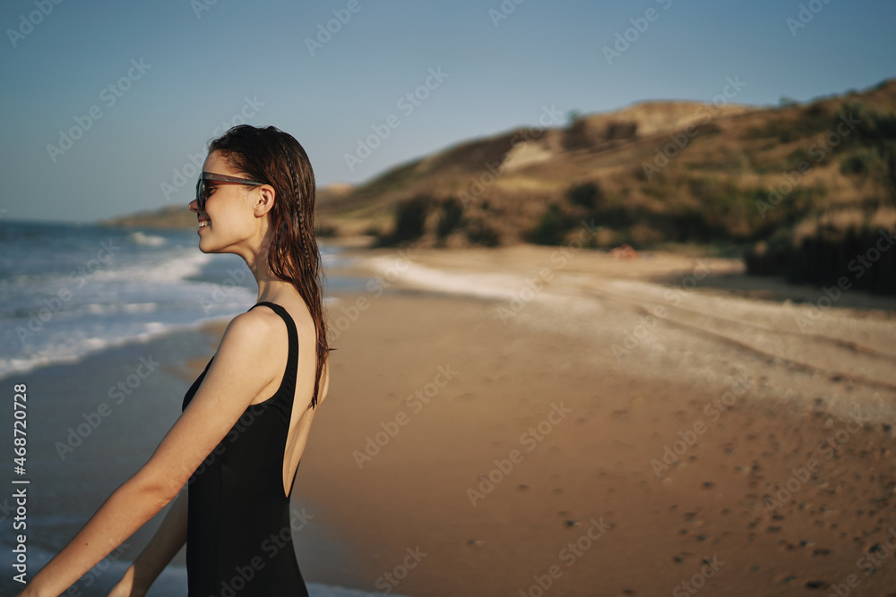 woman walks along the sandy shore in a black swimsuit sun tropics