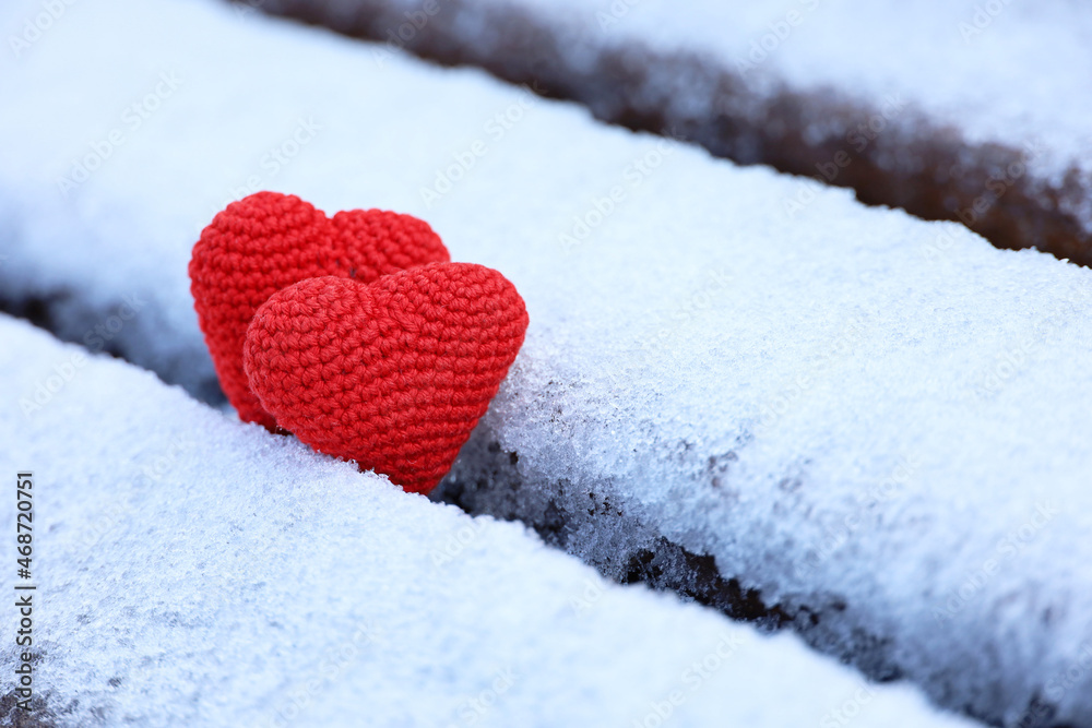 Couple of knitted red hearts in the snow on a park bench. Valentine's card, two symbols of love, background for romantic event in winter, Christmas celebration Couple of knitted red hearts in the snow on a park bench. Valentine's card, two symbols of love, background for romantic event in winter, Christmas celebration