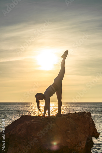 Girl gymnast is training on the beach by the sea sunset. Does twine. Photo series.