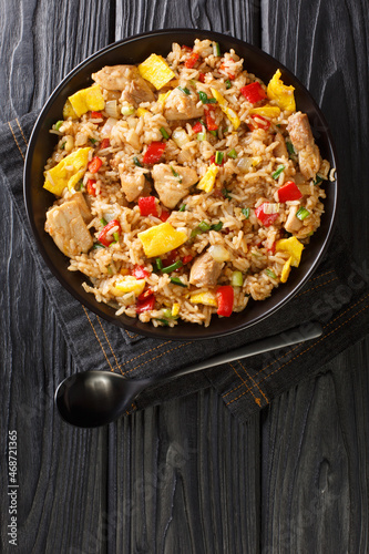 Arroz Chaufa is Peruvian Chinese fried rice consists of rice, red bell peppers, onions, garlic, soy sauce, scrambled eggs and chicken close up in the bowl on the table. Vertical top view from above photo