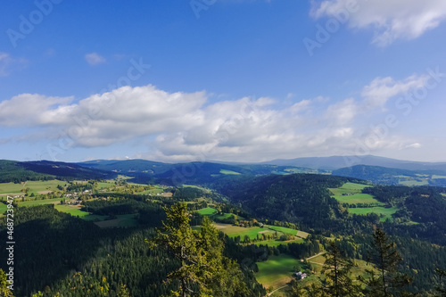 green landscape with fields forest and mountains with white clouds on the blue sky