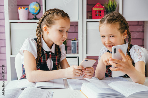 Two young female classmates are sitting at a desk and using smartphones. Modern technology concept. photo