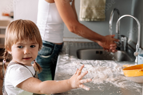 Candid portrait of little girl helps her mother to prepare cookies. Cute kid with flour in kitchen.