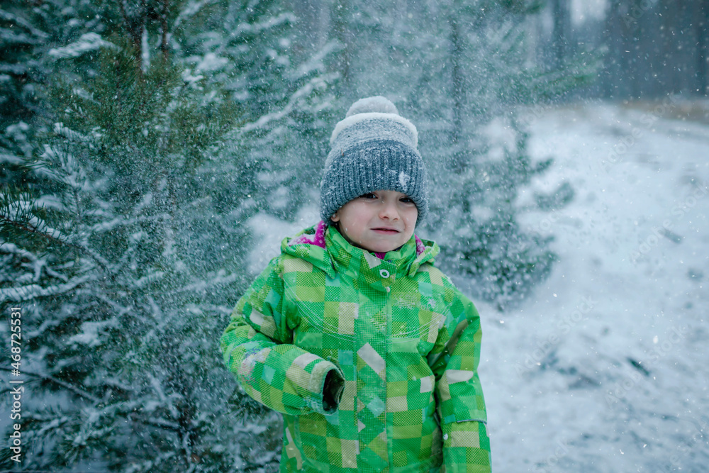 Frozen boy in warm clothes walks in forest with the first long-awaited snow, family active weekend, snowing day, outdoor lifestyle, winter wonderland Frozen boy in warm clothes walks in forest with the first long-awaited snow, family active weekend, snowing day, outdoor lifestyle, winter wonderland