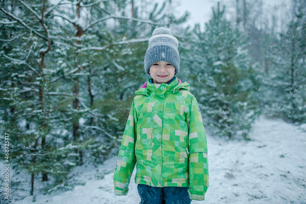 Little boy in warm clothes walks in forest with the first long-awaited snow, family active weekend, snowing day, outdoor lifestyle, winter wonderland