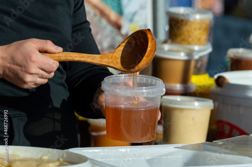 a man puts honey in a plastic container with a wooden spoon