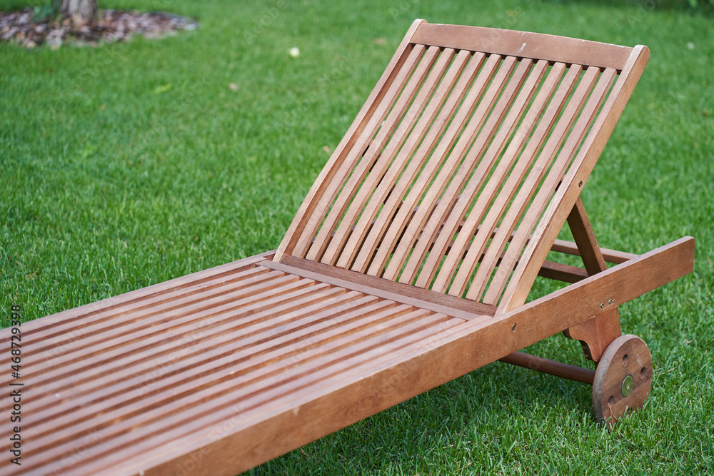 Close-up of a wooden chaise longue in a fresh garden on green grass.The concept of relaxation, tanning in the backyard. High quality photo Close-up of a wooden chaise longue in a fresh garden on green grass.The concept of relaxation, tanning in the backyard. High quality photo