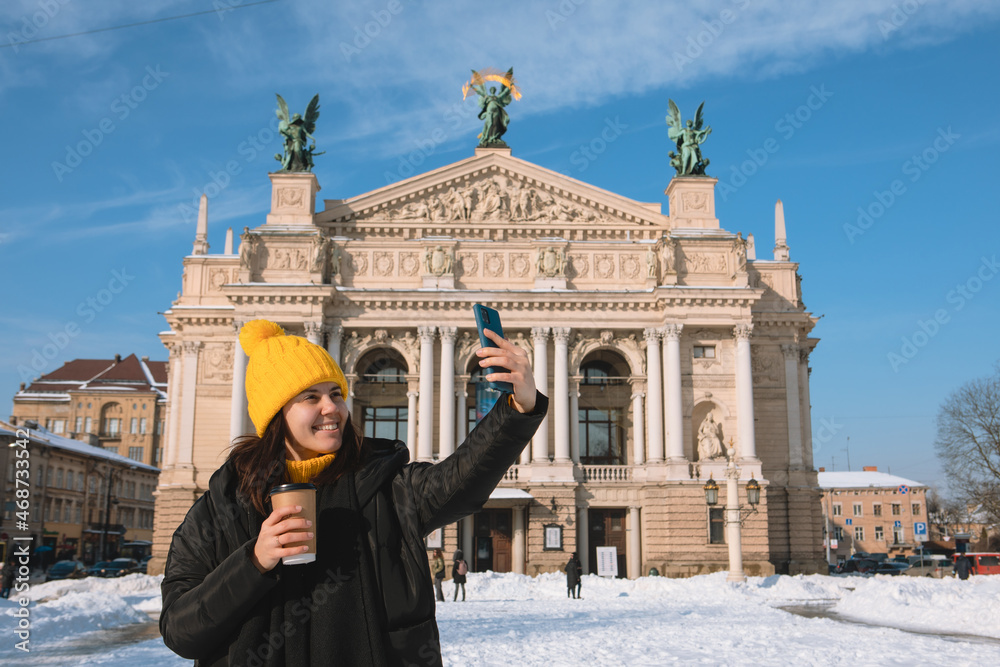 woman traveler drinking coffee to go taking selfie in front of opera building