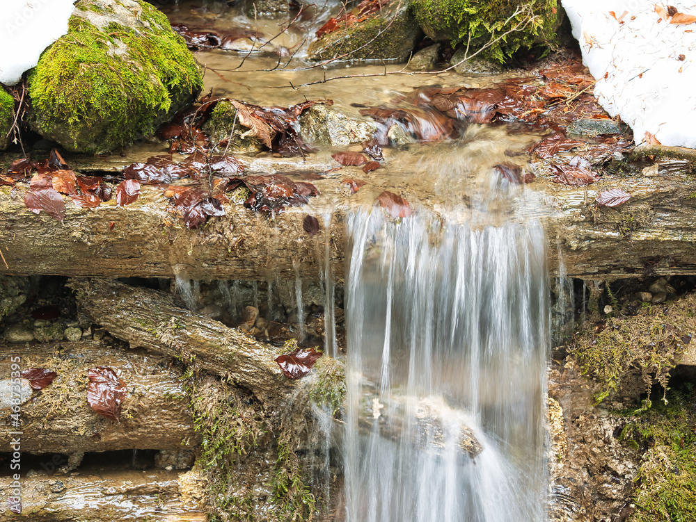 Fototapeta premium Small artificial waterfall. Water of a mountain stream flowing over wooden sill. Seen in the municipality of Schwarzenberg in the canton of Lucerne in Switzerland
