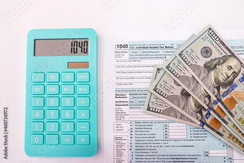 tax forms 1040 with dollars and calculator on white background. View from above .
