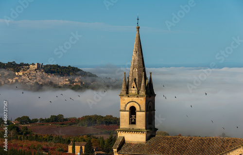 view of church tower at Bonnieux hiitop village in  provence  France with Lacoste in the background misty autumn morning seen from the luberon mountain . photo