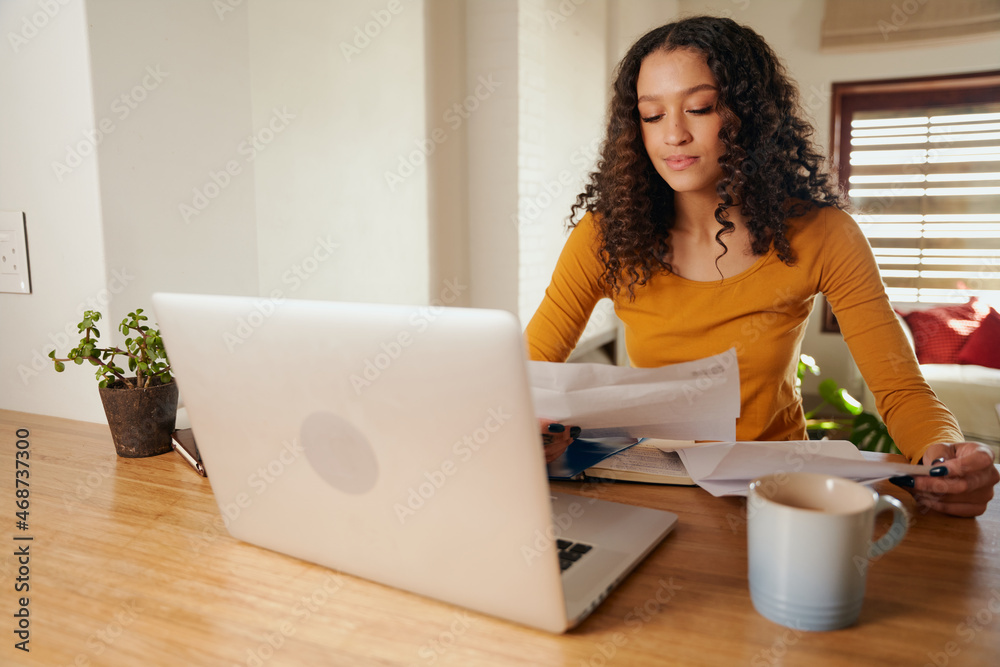 Multi-cultural female paying bills from home. Young professional remote working with laptop in modern apartment Multi-cultural female paying bills from home. Young professional remote working with laptop in modern apartment