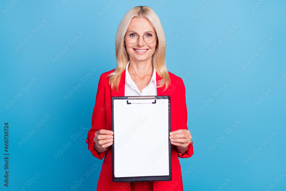 Photo of senior lady show empty space clip board documents investor banker isolated over blue color background Photo of senior lady show empty space clip board documents investor banker isolated over blue color background