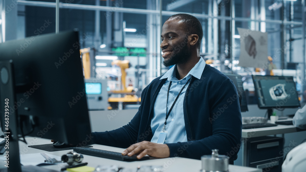 Car Factory Office: Portrait of Confident Black Male Chief Engineer Working on Desktop Computer. Professional Technician in Automated Robot Arm Assembly Line Manufacturing High-Tech Electric Vehicles