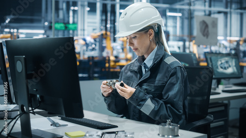 Car Factory Office: Portrait of Confident Female Chief Engineer Wearing Hard Hat Working on Desktop Computer. Technician in Automated Robot Arm Assembly Line Manufacturing High-Tech Electric Vehicles