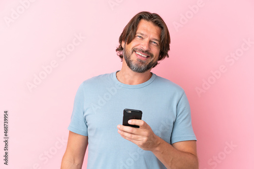 Senior dutch man isolated on pink background using mobile phone © luismolinero