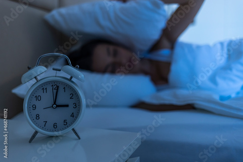 Sleepless and desperate beautiful woman awake at night not able to sleep looking at clock suffering from insomnia in sleep disorder concept. Woman suffering from insomnia. Blue night time effect