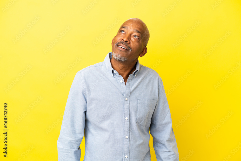 Cuban Senior isolated on yellow background looking up and with surprised expression Cuban Senior isolated on yellow background looking up and with surprised expression