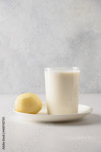 Vegan potato milk in glass and potato in bowl on white background. Vertical format. Close up. Plant based milk replacer and lactose free.