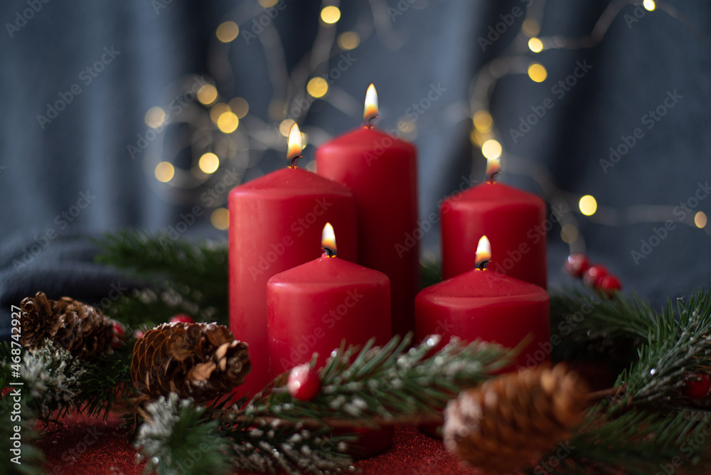 Christmas decoration with red candles, spruce branches, cones and garland on red table on blurry background. Side view. New year mood, festive concept, holiday table, gift card.