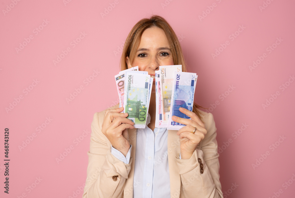 Photo of pretty smiling business woman standing isolated over pink background holding money. Photo of pretty smiling business woman standing isolated over pink background holding money.