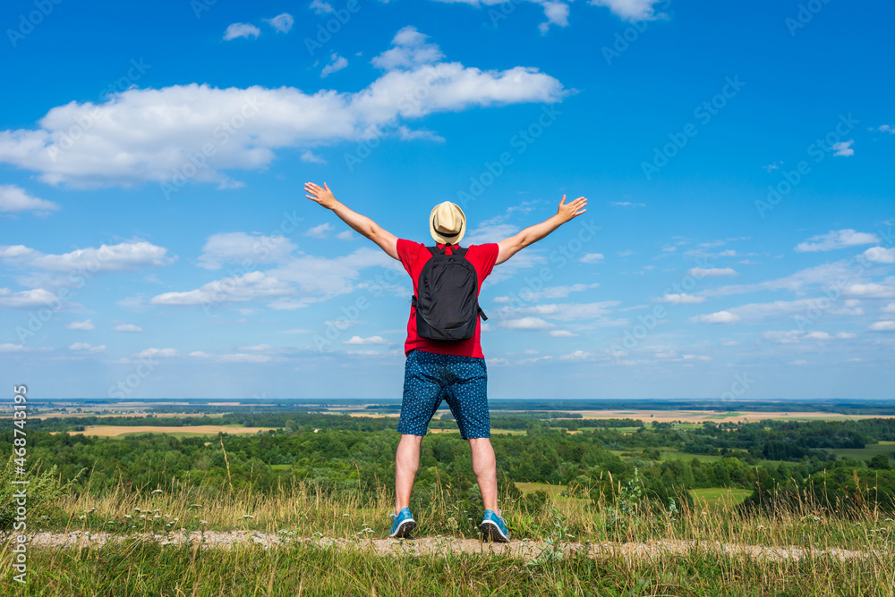Tourist man with backpack enjoying the view in nature.Traveler man with backpack,arms outstretched stand on blue sky. Tourist man with backpack enjoying the view in nature.Traveler man with backpack,arms outstretched stand on blue sky.