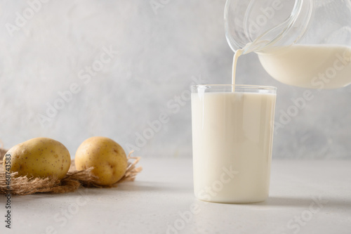 Obraz na plátně Pouring vegan potato milk in glass and potato in bowl on light background