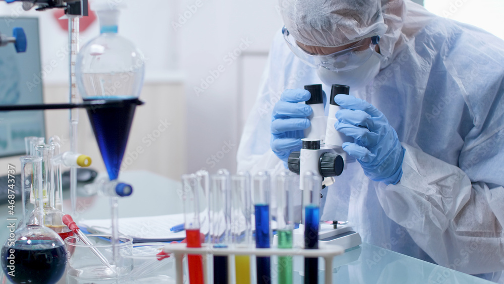 Fototapeta premium Closeup of scientist chemist doctor wearing ppe equipment analyzing sample with virus using medical microscope during microbiology experiment in hospital laboratory. Medicine concept