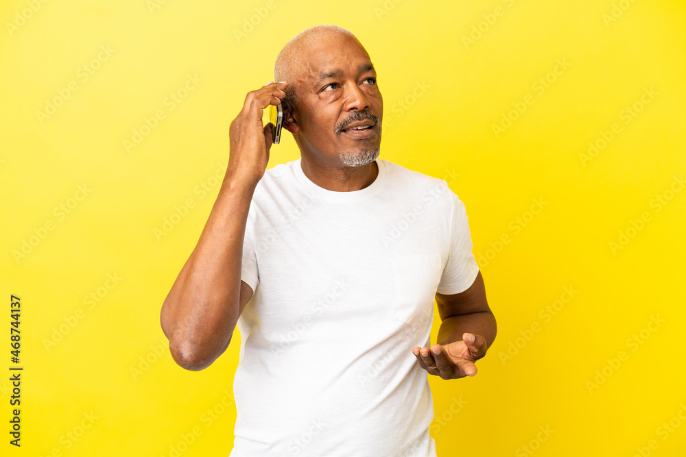 Cuban Senior isolated on yellow background keeping a conversation with the mobile phone with someone Cuban Senior isolated on yellow background keeping a conversation with the mobile phone with someone