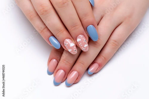 Blue French manicure with painted clouds and crystals on a close-up of long oval nails on a white background. Gel nails. 