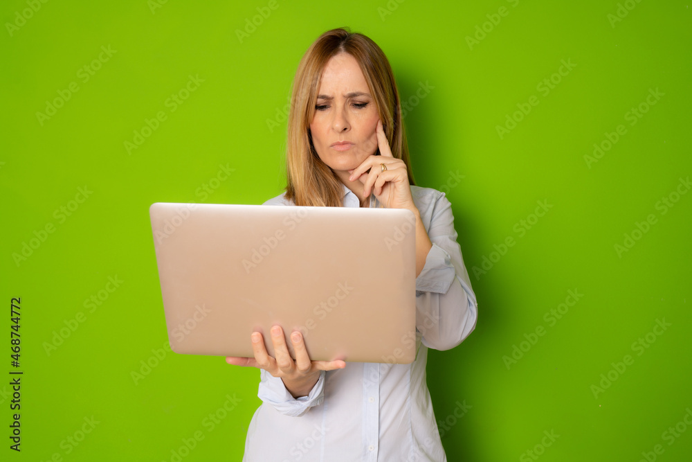 Portrait of young pensive businesswoman holding silver laptop in the office isolated over green background Portrait of young pensive businesswoman holding silver laptop in the office isolated over green background