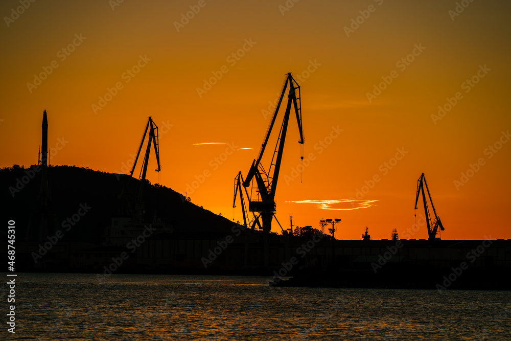 Port shipyard cranes against orange sky, Ferrol, Galicia, Spain