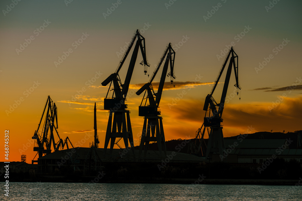 Shipyard crane silhouettes against orange dusk sky