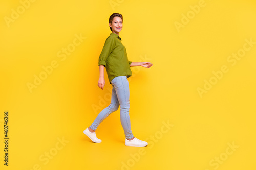 Photo of cheerful positive carefree lady walk wear green shirt jeans shoes isolated yellow color background © deagreez
