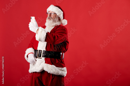 Santa Claus taking a selfie with a mobile phone on red background