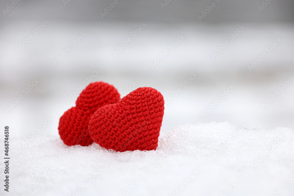 Fototapeta premium Love hearts in the snow in a park. Valentine's card, two red knitted symbols of love, background for romantic event in winter, Christmas celebration