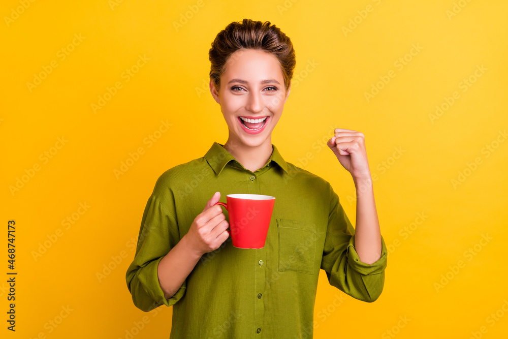 Photo of cheerful lady hold cup celebrate victory raise fist wear green shirt isolated yellow color background Photo of cheerful lady hold cup celebrate victory raise fist wear green shirt isolated yellow color background