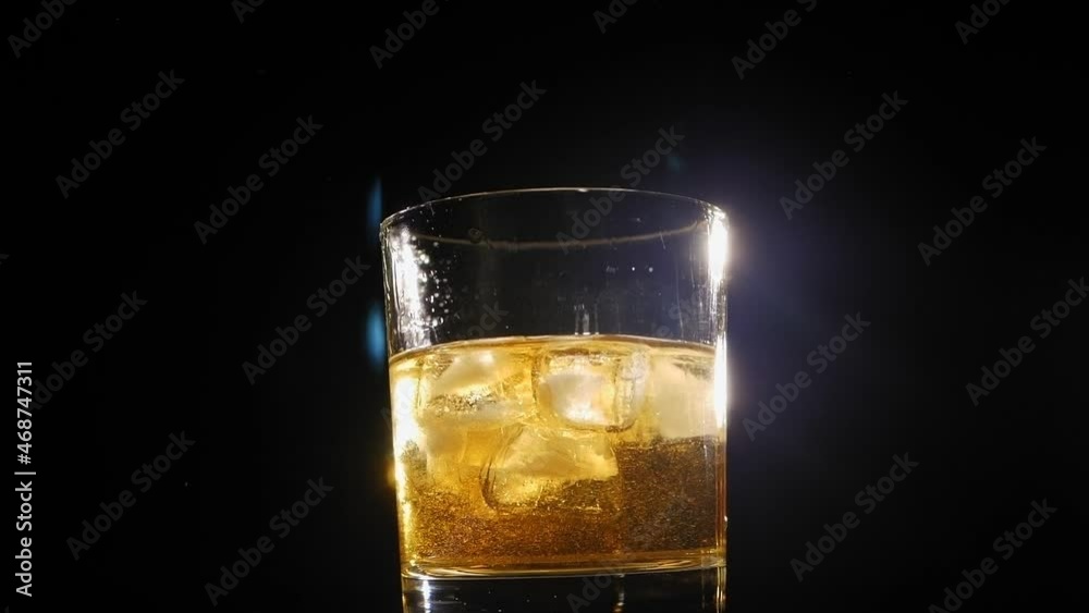 Close-up of a misted glass of chilled single malt whiskey and ice spinning around on a black background. Macro shot. Slow motion. Close-up of a misted glass of chilled single malt whiskey and ice spinning around on a black background. Macro shot. Slow motion.