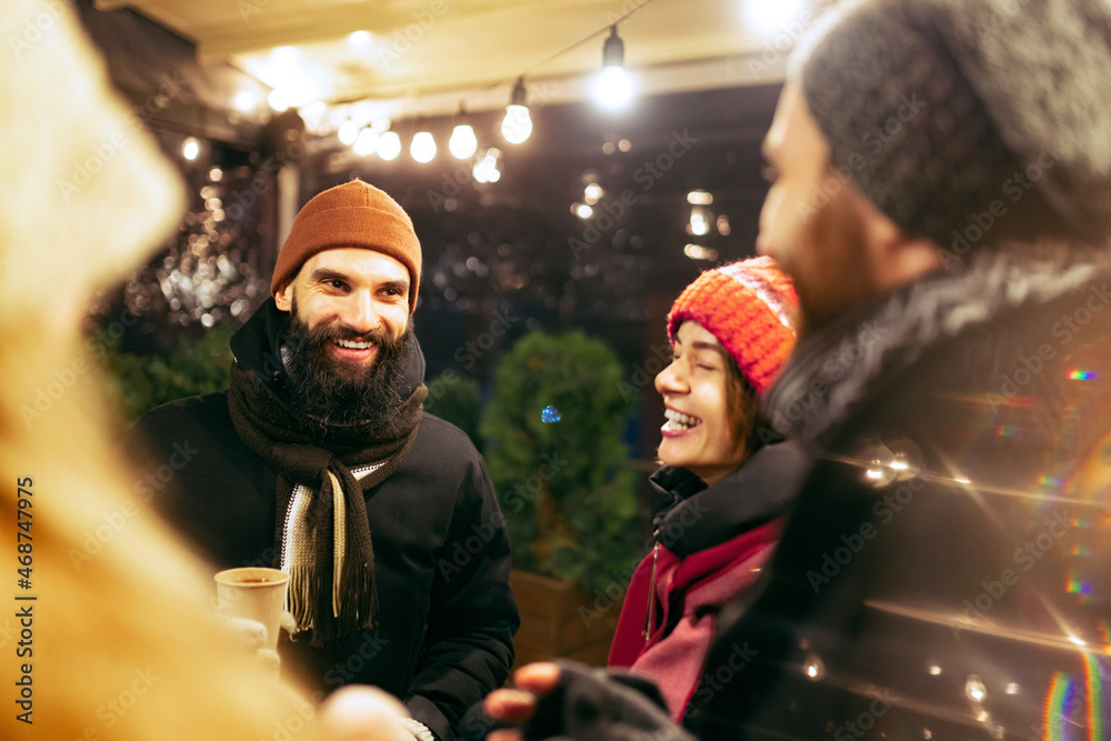 Close-up happy smiling friends with cups of mulled wine spending time together at winter fair at evening. Holidays, Christmas concept