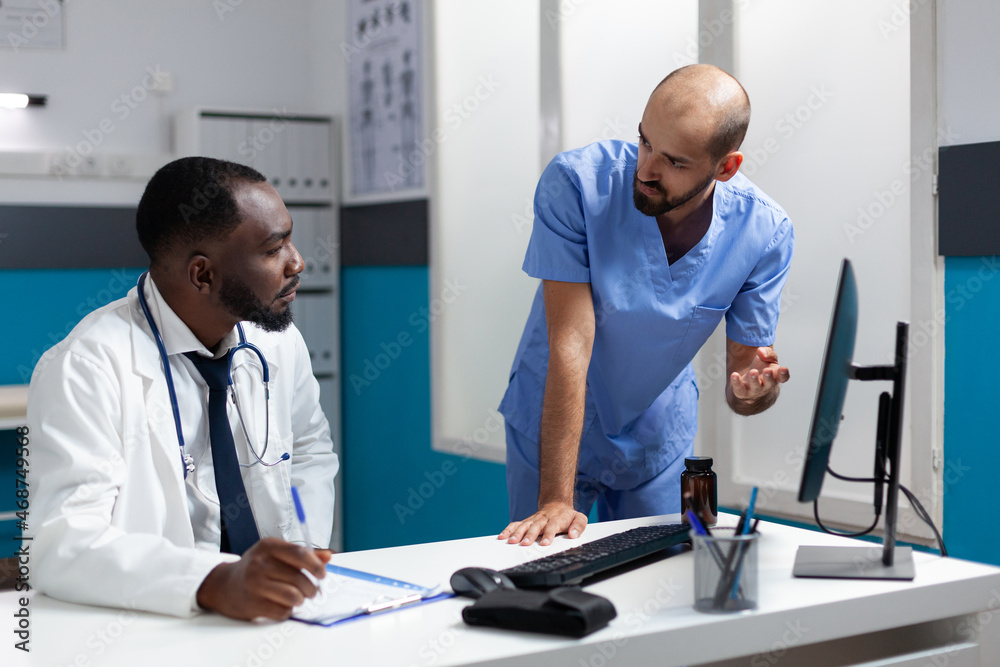 African american physician doctor analyzing clinical documents discussing healthcare treatment with man nurse. Medical team working in hospital office monitoring disease symptoms during appointment