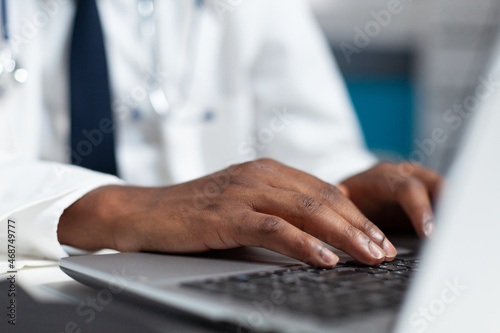 Closeup of african american doctor hand typing medical prescription after analyzing patient sickness expertise. Therapist man working at healthcare treatment in hospital office. Medicine service
