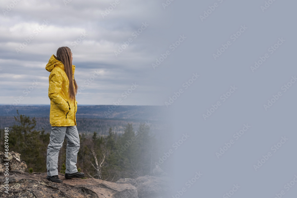 Obraz premium A tourist in a yellow jacket and gray pants stands on the top of a mountain and admires the beauty of nature. There is a place for your text.