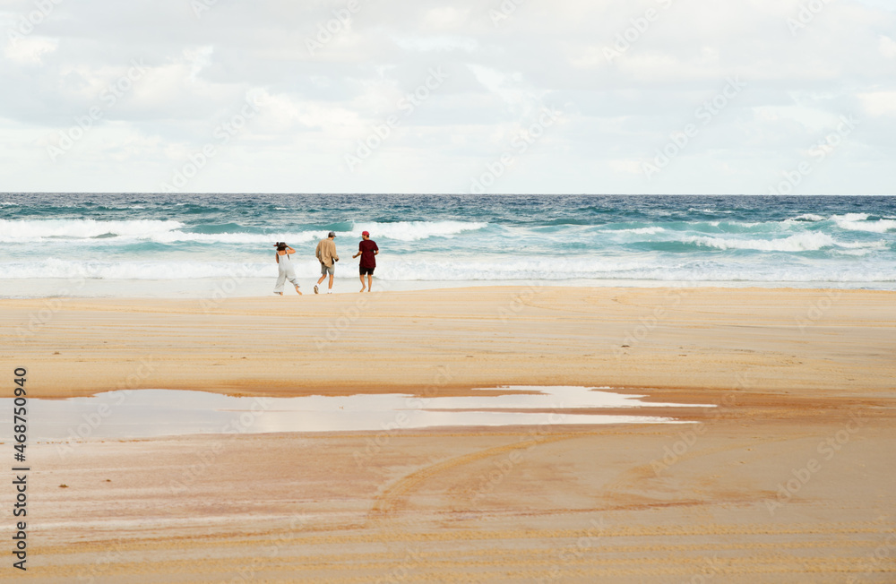 Rear View of Three Friends Walking and Talking on a Beach with the Ocean as Background